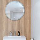 Round mirror above a sink with wood effect wall tiles and white cabinet