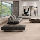 Modern living room with grey sofa and ottoman, abstract wall art and beige floor tiles.