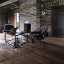 A rustic living room scene with dark wooden flooring, exposed brick walls, two accent chairs and a wooden coffee table on a cowhide rug.