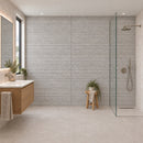 A modern bathroom with light grey textured tiled wall and large grey floor tiles, a glass shower enclosure, a wall hung wood vanity with a white basin and small potted plants.