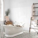 White freestanding bathtub in a modern bathroom with a ladder shelf, white wall tiles and decorative tiled floor.