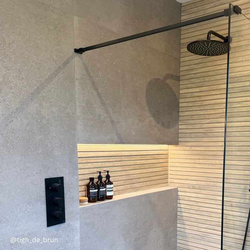 Shower with large grey concrete effect wall tiles and recess shelf with wood effect tiles.