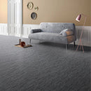 Textured charcoal fabric effect floor tiles with a light gray sofa, a pink floor lamp, and a small tray on the floor.