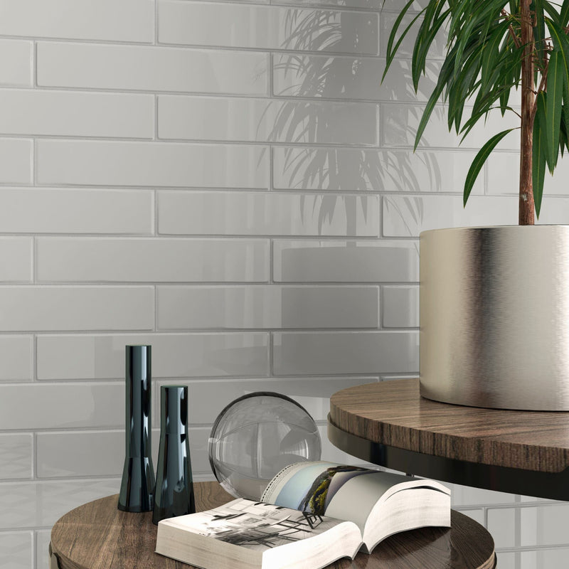 Modern interior design with a book, vase, and plant against a light grey tiled wall.