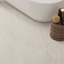 Close-up of a white marble effect tiled bathroom floor with a wooden stool and decorative items.