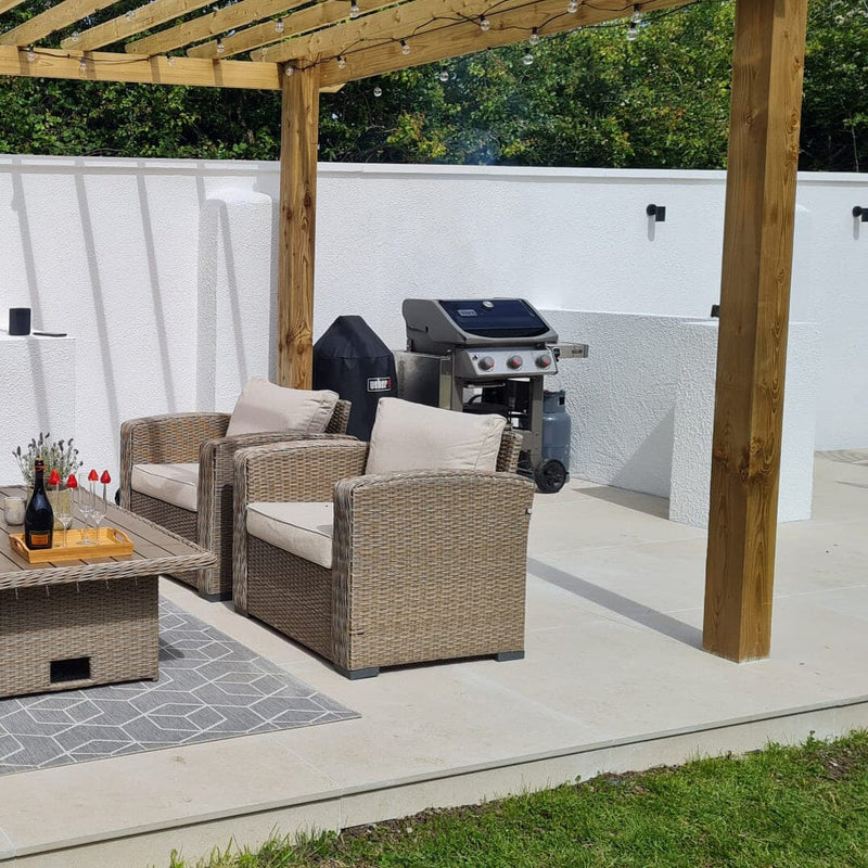 Outdoor patio with wicker chairs, coffee table, and barbecue on large beige paving slabs.