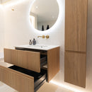 Bathroom with wooden vanity units, round mirror and brushed brass tap.