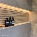 Three bottles of Aesop products on a shelf with wooden and concrete effect wall tiles.