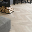 Wood effect luxury vinyl floor with a herringbone pattern, grey ottoman and stacked fire logs.