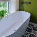 White freestanding bathtub in a bathroom with green wall and patterned tiles.