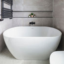 Modern bathroom with a freestanding white bathtub against a gray tiled wall.