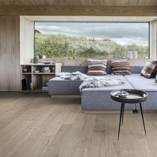 Modern living room with a large sofa, wooden floor and scenic window.