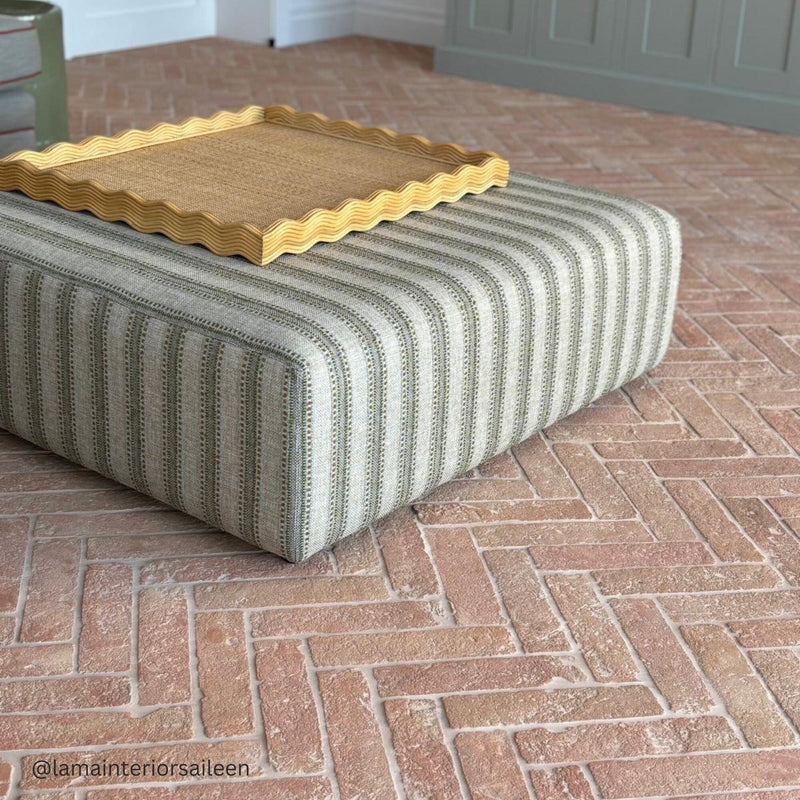 Striped ottoman with a rattan tray on a terracotta floor