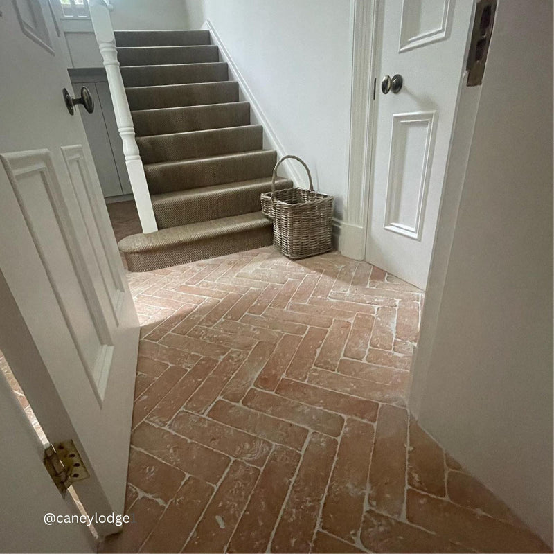 Hall with terracotta flooring, carpeted staircase, and a basket.