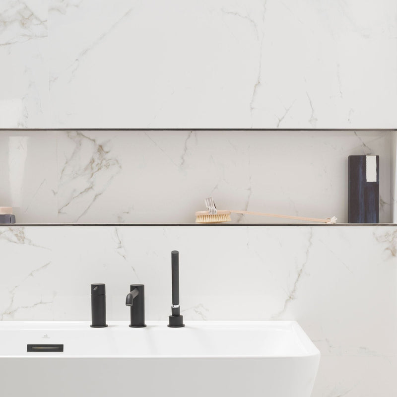 Bath with marble effect wall tiles and a black tap.
