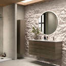 Modern bathroom with feature wall with textured stone, round backlit mirror and dark wooden cabinets.