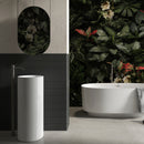 bathroom with freestanding bath and plants and black fluted wall tiles behind tall basin.