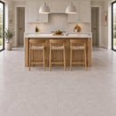Light taupe stone effect floor tiles in a modern kitchen setting, shown in a bright, contemporary kitchen with a wooden island, three bar stools, pale cabinets, and two pendant lights.