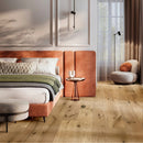 Light oak wood flooring in a modern, warm-toned bedroom setting with a bed and terracotta coloured headboard, round side table and boucle armchair.