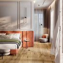 A modern bedroom interior with light oak wood flooring, featuring a bed with an orange-brown headboard, neutral bedding, a small side table, a round accent chair, and sheer curtains.
