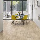 Dining area with a large window, round table and yellow dining chairs and pale engineered wood flooring laid in a Dutch pattern.