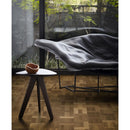 Wooden side table and leather seat in front of a large window and dark engineered wood flooring laid in a Dutch pattern.