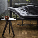 Wooden side table and leather seat with dark engineered wood flooring laid in a Dutch pattern.
