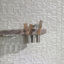 Textured wall tiles with a shelf holding glasses and kitchen utensils.