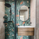 Bathroom with tropical floral wallpaper, shower, wood effect vanity and oval mirror.