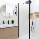 Modern bathroom with wooden vanity, round mirror, matt black fixtures and white marble effect wall tiles.