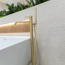 Brushed brass floor standing bath mixer tap and beige textured wall tiles.