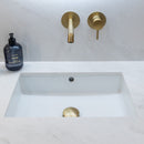 Bathroom vanity with white countertop, square sink and brushed brass wall mounted tap.