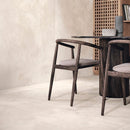 Dark wood dining room table and chairs with large beige concrete effect wall and floor tiles.