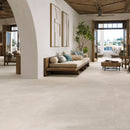 A bright living room with large light beige stone-look floor tiles, a low wooden daybed and an open-air balcony view.