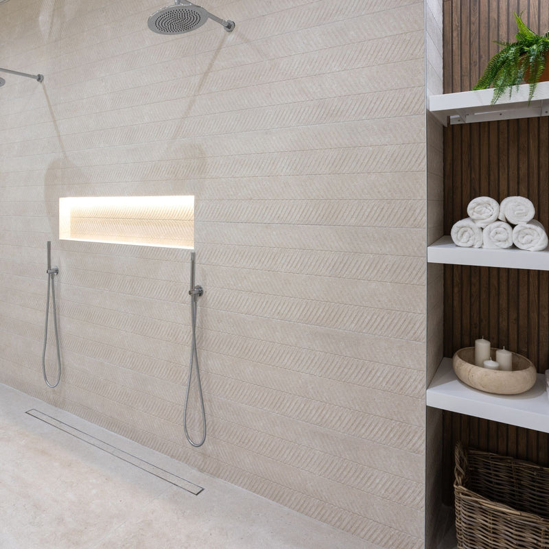 Shower with textured beige wall tiles, recess shelf and shelves with towels and candles.