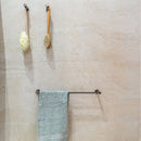 Towel rail with a green towel, soap dish, and brush holder on a beige stone effect tiled wall.